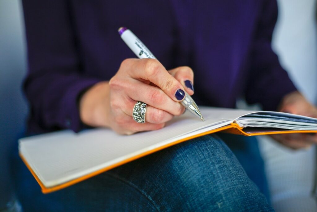 Someone writing in a notepad which is resting on their knee