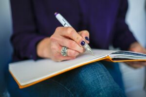 Someone writing in a notepad which is resting on their knee