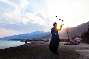 A woman juggling three balls in the air, stood on a beach